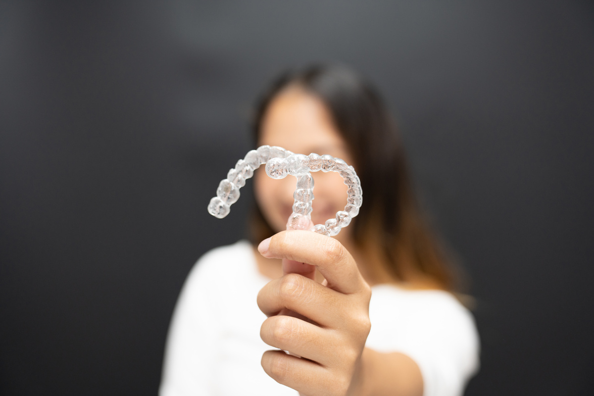 Women hand hold inivisalign braces, transparent aligner, invisible retainer or orthodontic silicone trainer with blur mile in background. A way to have a beautiful smile.