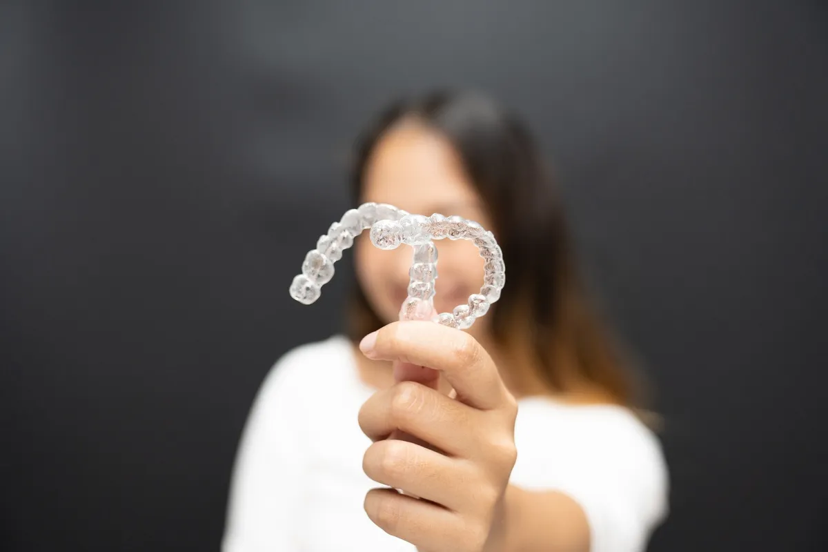 Women hand hold inivisalign braces, transparent aligner, invisible retainer or orthodontic silicone trainer with blur mile in background. A way to have a beautiful smile.
