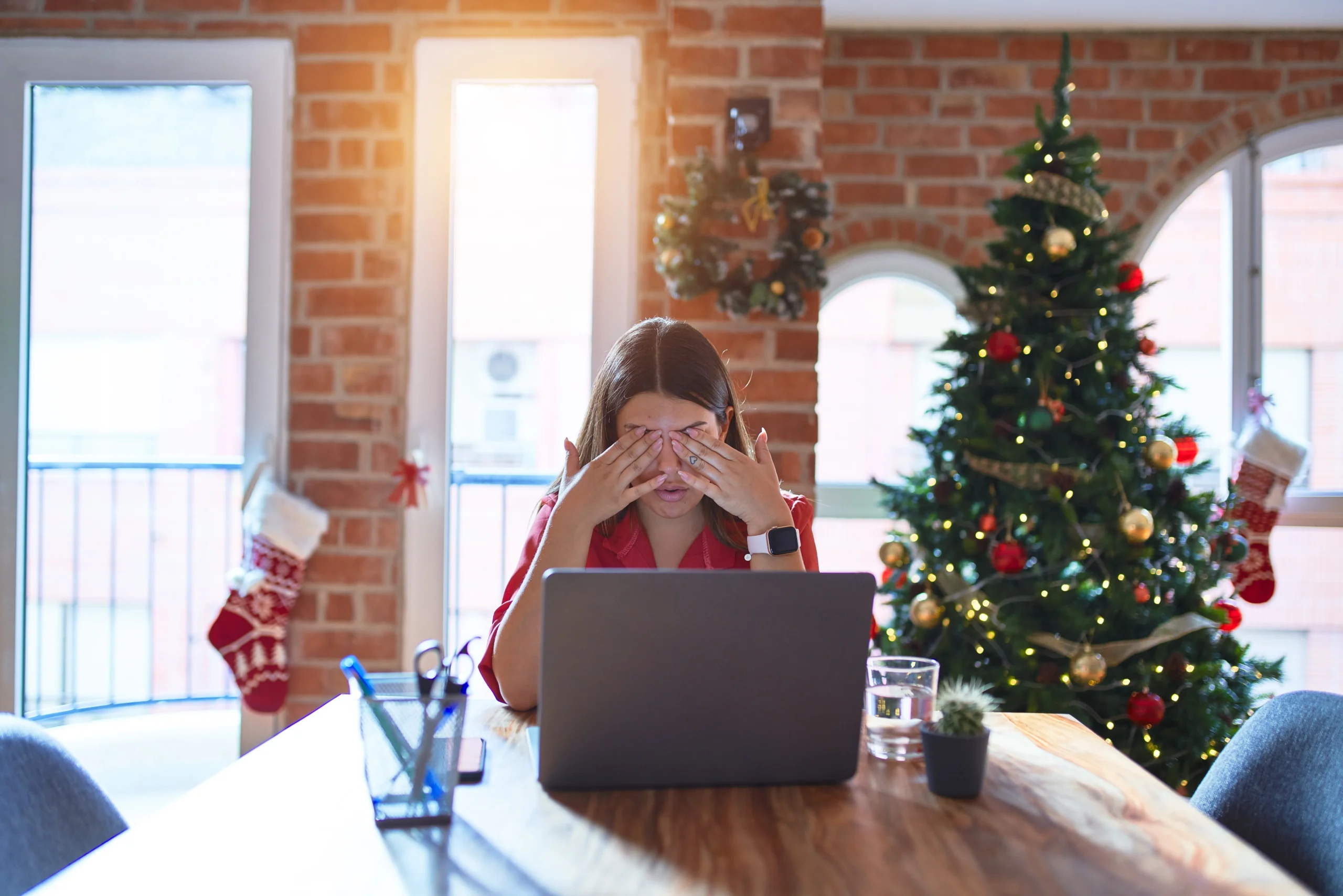 Beautiful woman sitting at the table working with laptop at home around christmas tree rubbing eyes for fatigue and headache, sleepy and tired expression. Vision problem