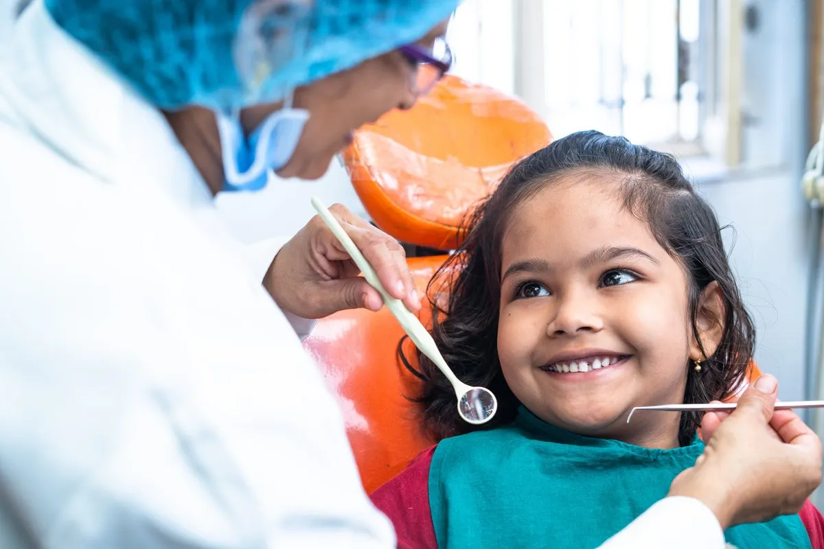 happy smiling kid looking at dentist while treating at hospital - concept of dental care, expertise and friendly hygienist.