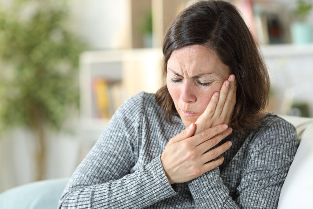 Middle age woman in pain suffering toothache touching face sitting on a couch at home