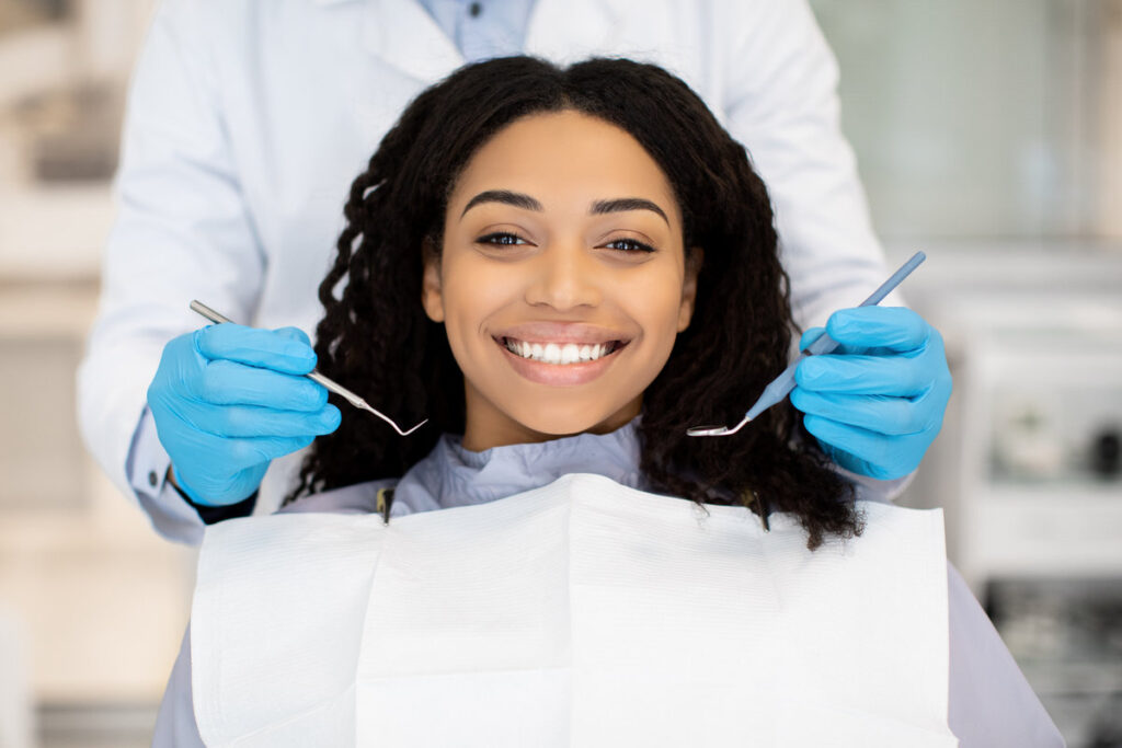 Portrait Of Happy Young Black Woman Having Check Up At Dental Clinic, Closeup Shot Of Millennial African American Female Patient Getting Teeth Treatment With Dentist In Modern Stomatologic Cabinet